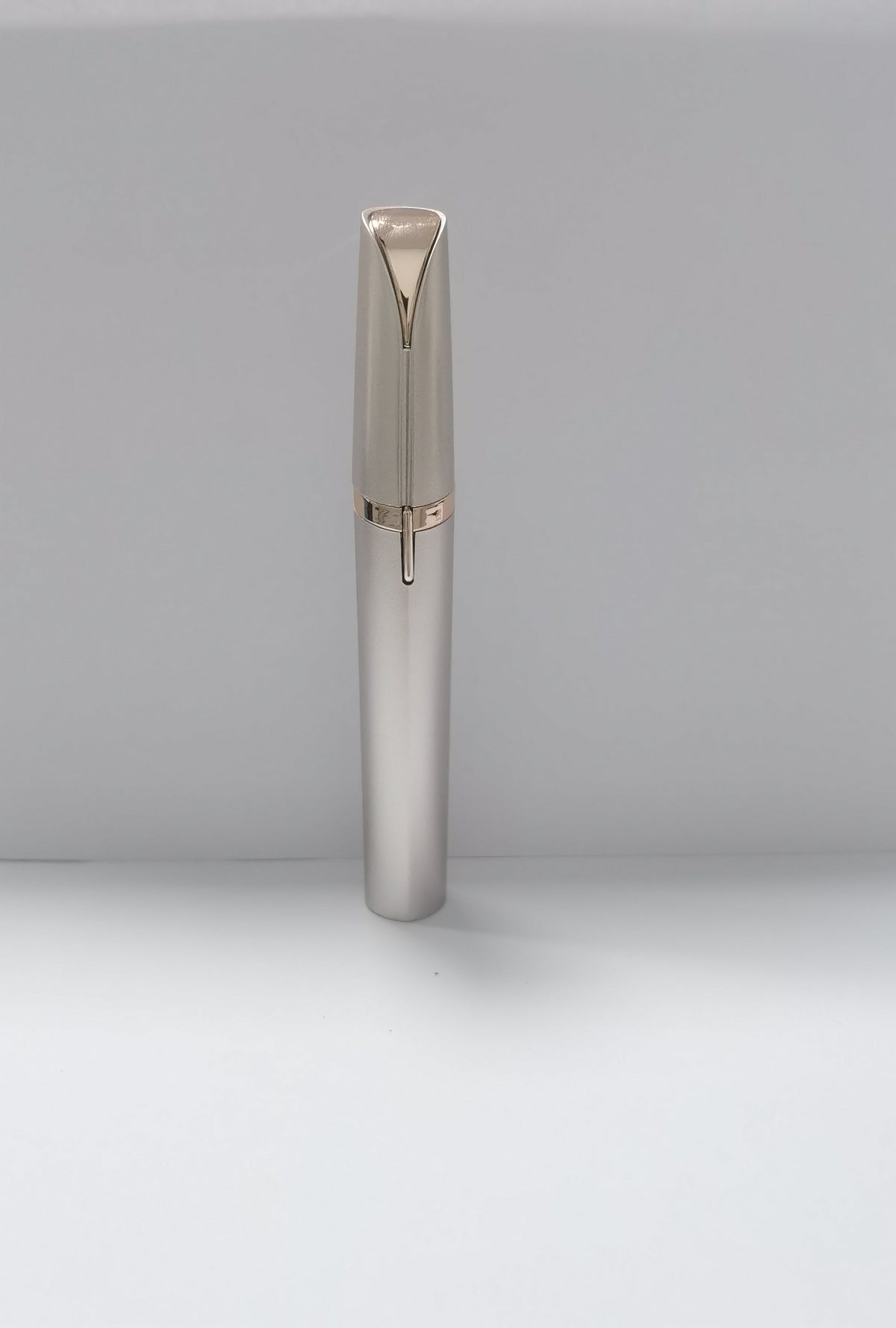 A sleek, metallic silver pen with a gold accent ring and a gold-toned clip, standing upright on a light gray surface against a neutral gray background.