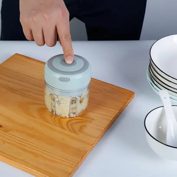 Hand pressing a button on a small kitchen appliance on a wooden cutting board with a neutral background.