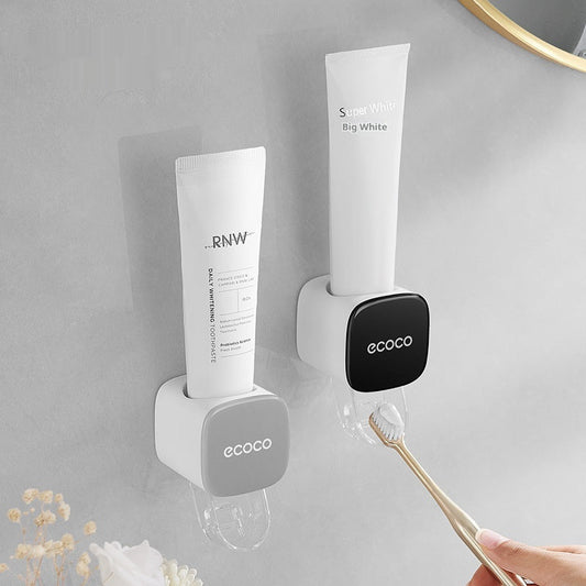 Wall-mounted toothbrush holder with toothpaste dispenser on a gray wall.