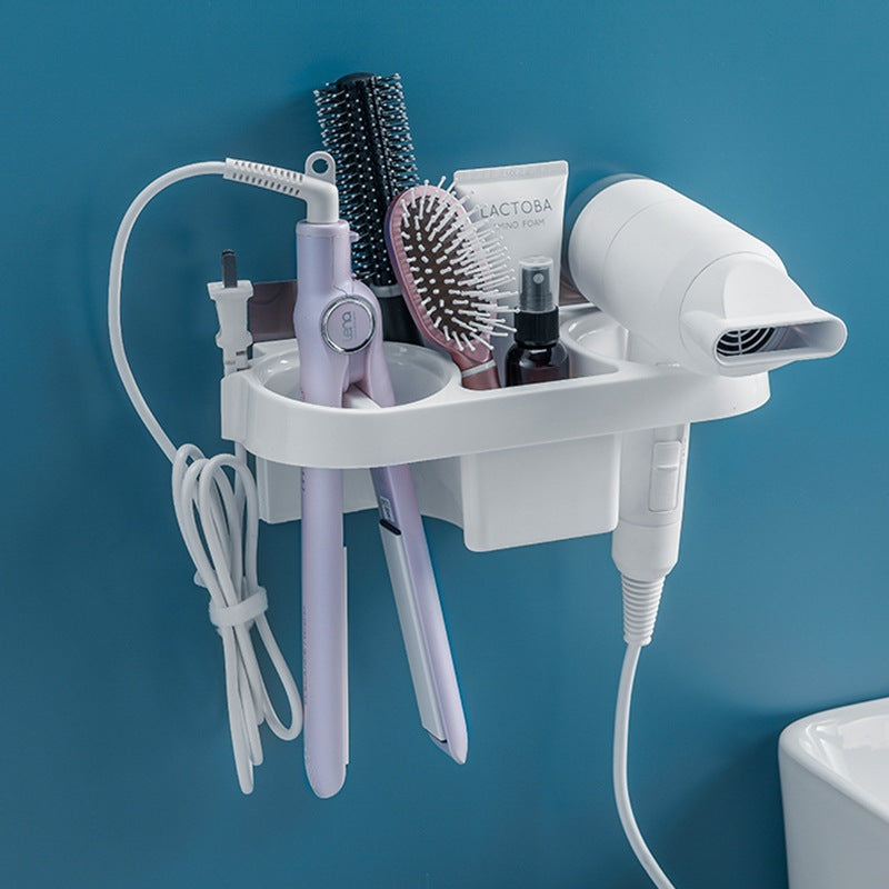 A white wall-mounted hair dryer organizer holding a white hair dryer, lavender styling tools, a black hairbrush, a pink bristle brush, and a small bottle, mounted on a blue wall.