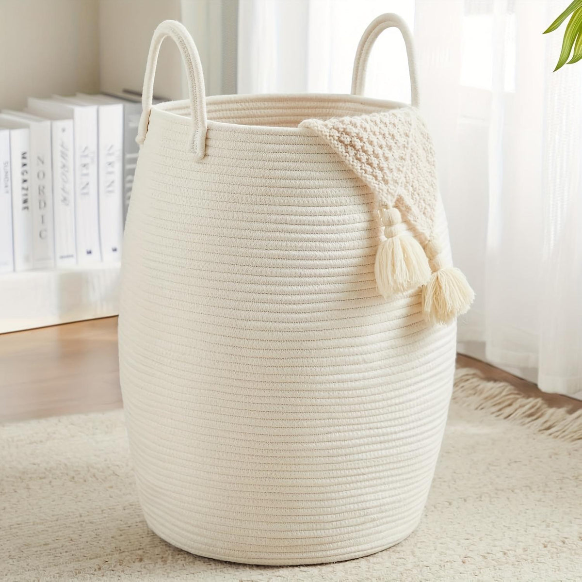 Beige woven basket with tassels on a light wooden floor.