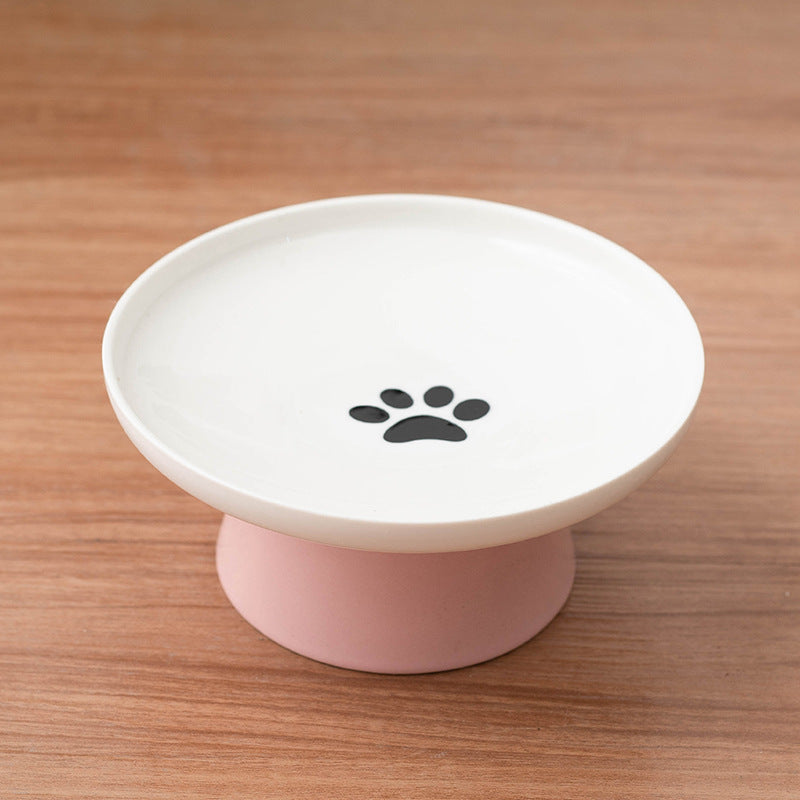 White elevated pet feeder with pink base and black paw print on a wooden surface