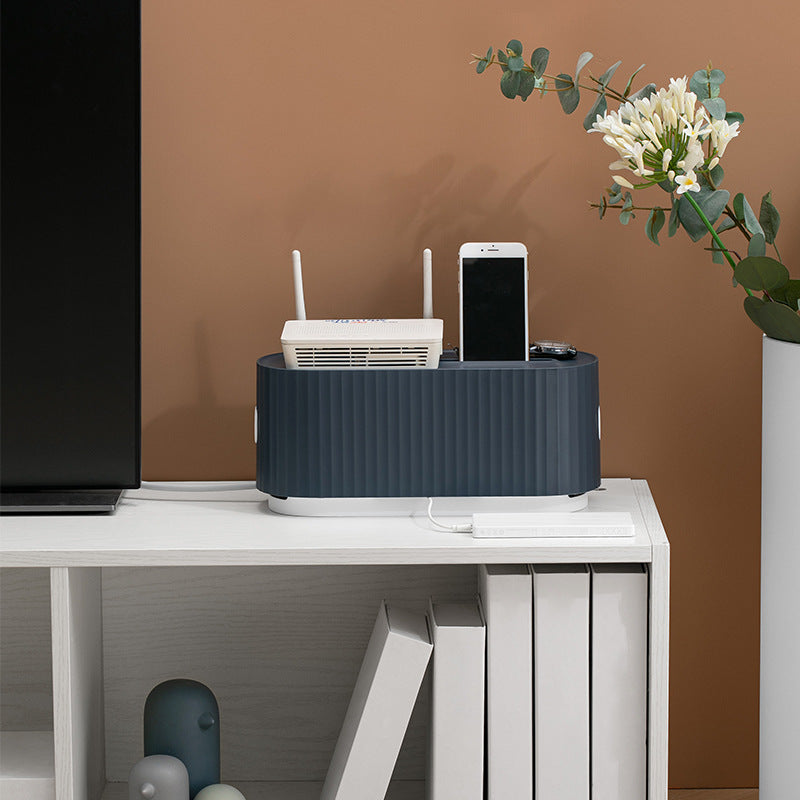 Desk with a black cable management box, router, and smartphone against a brown wall.