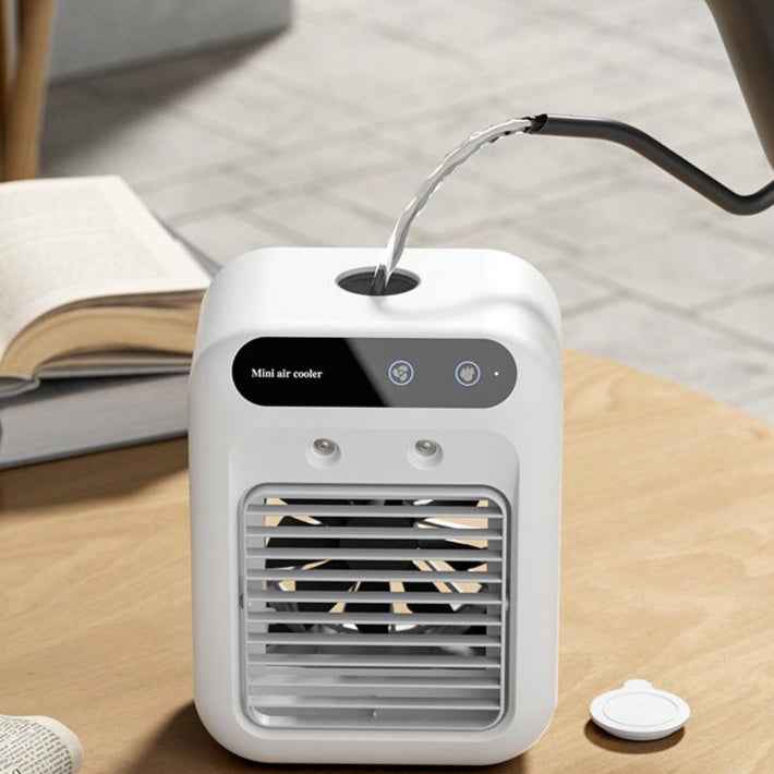 White portable air cooler on a wooden surface with a book and remote control in the background.