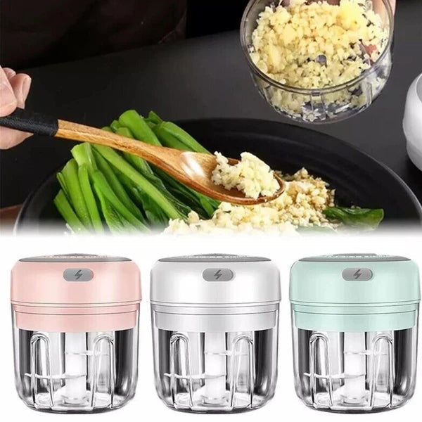 Three small food choppers in pink, silver, and green with a blurred background of food preparation.