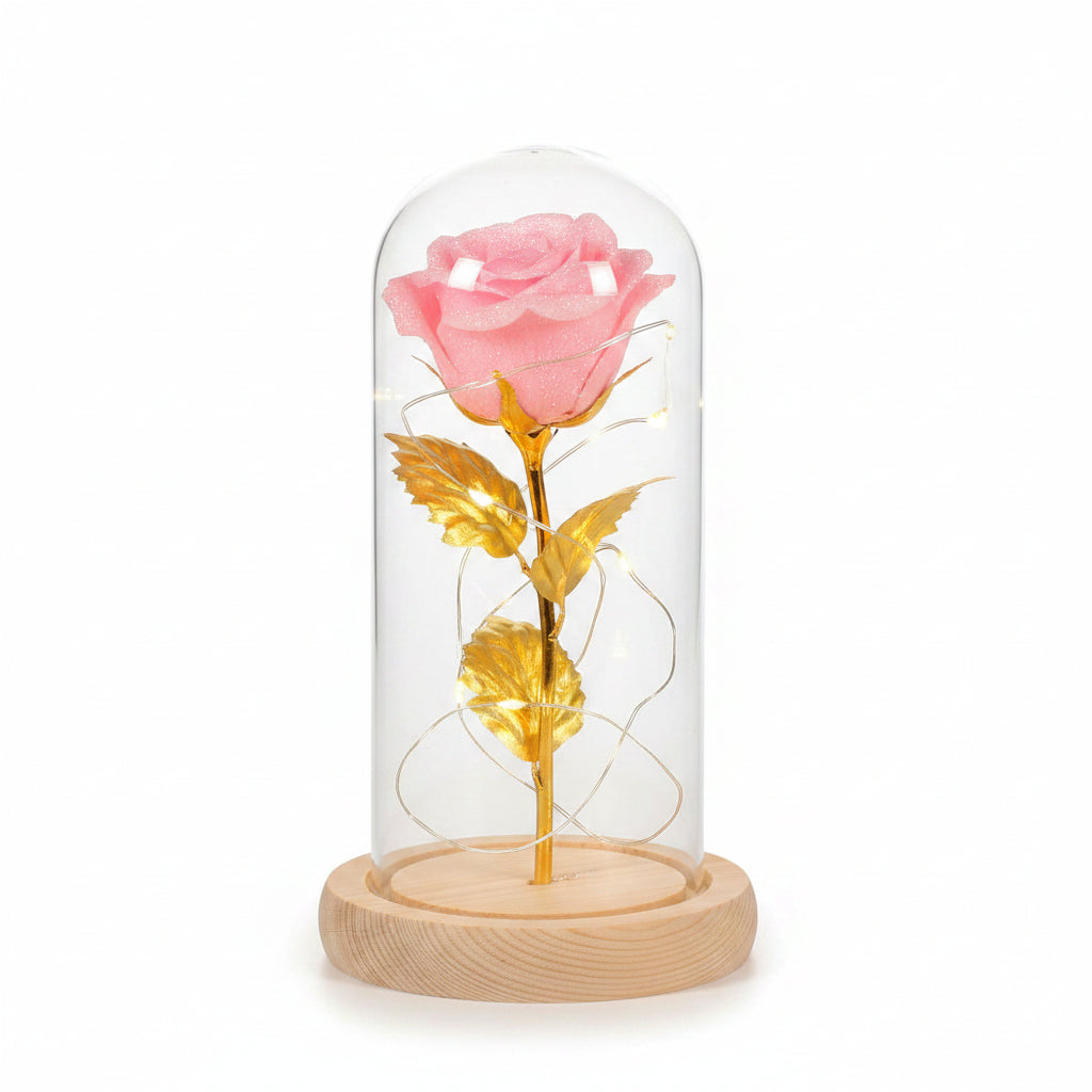 Pink and gold rose in a glass dome with LED lights on a wooden base, placed on a surface with a blurred background.
