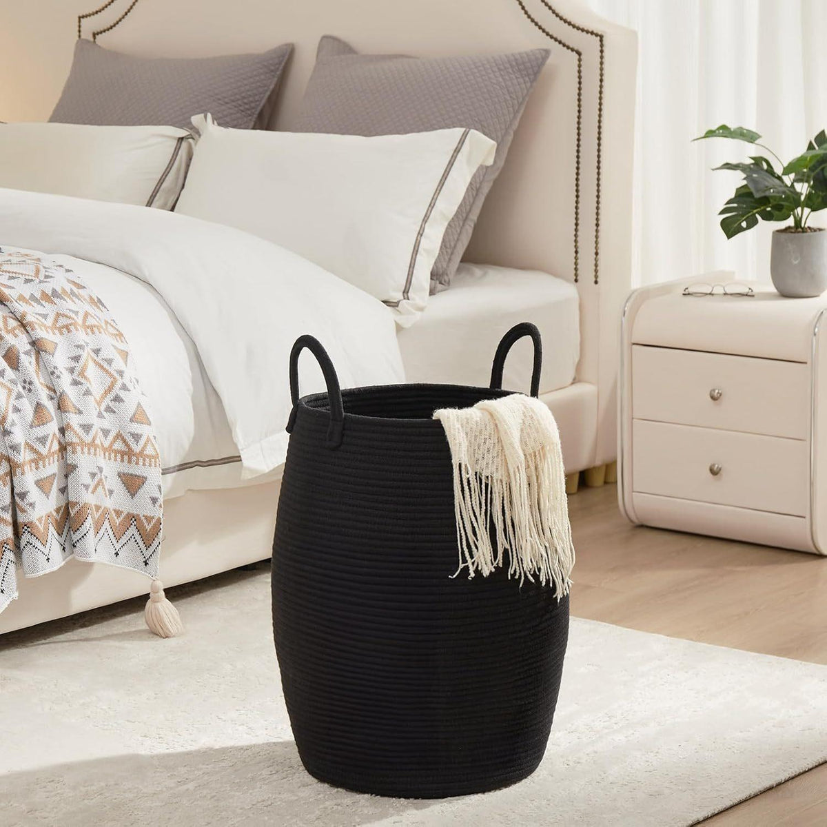 Black woven basket with a white blanket on a rug in a bedroom setting.