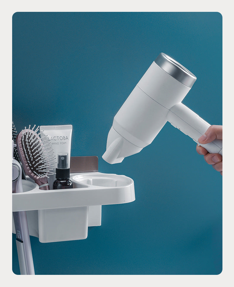 A white hair dryer with a silver nozzle attachment is being used to dry a hairbrush and other bathroom accessories on a white wall-mounted holder against a blue background.
