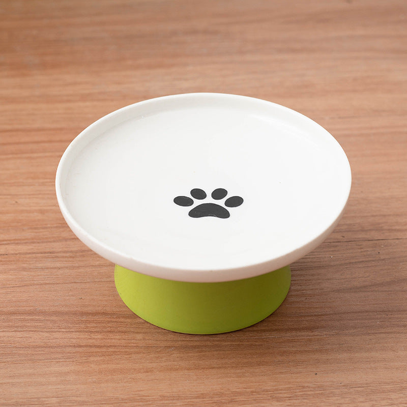 White elevated pet feeder with green base and black paw print on a wooden surface