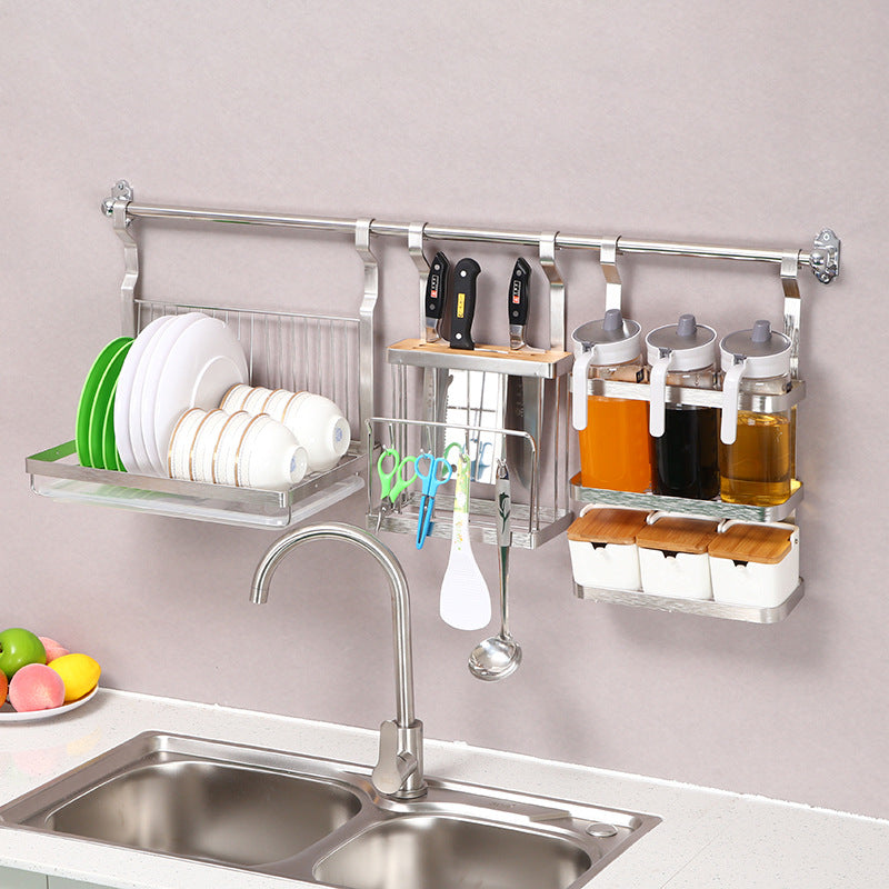 A wall-mounted stainless steel kitchen organizer rack hanging above a sink, holding plates, bowls, knives, spice jars, and utensils against a light wall.