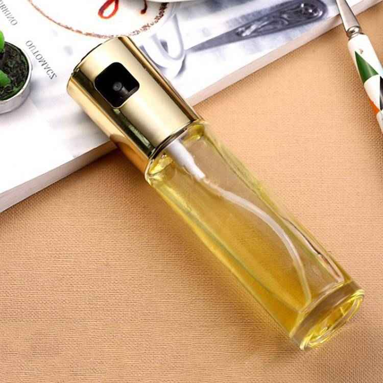 Glass spray bottle with gold nozzle on a beige surface