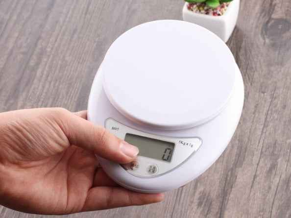 Digital kitchen scale held by a hand on a wooden surface