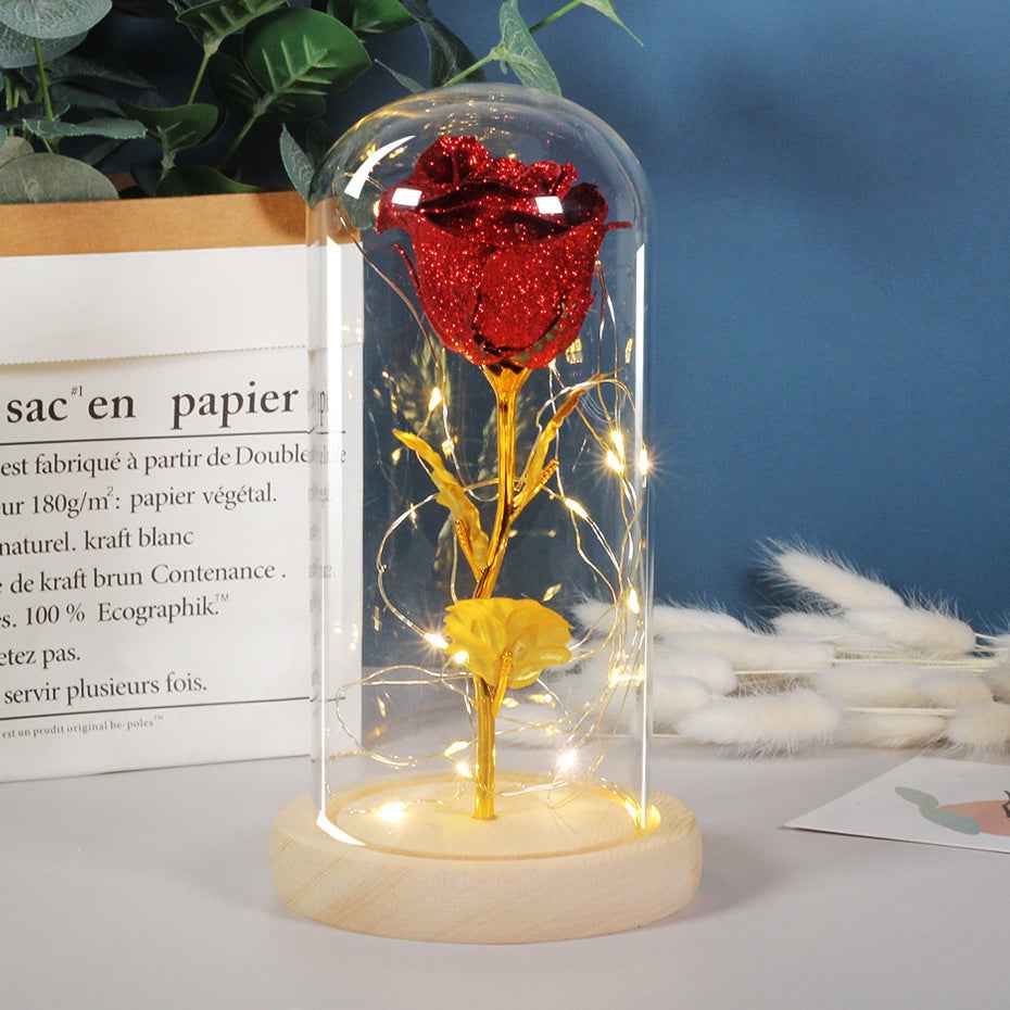 Red and gold rose in a glass dome with LED lights on a table.