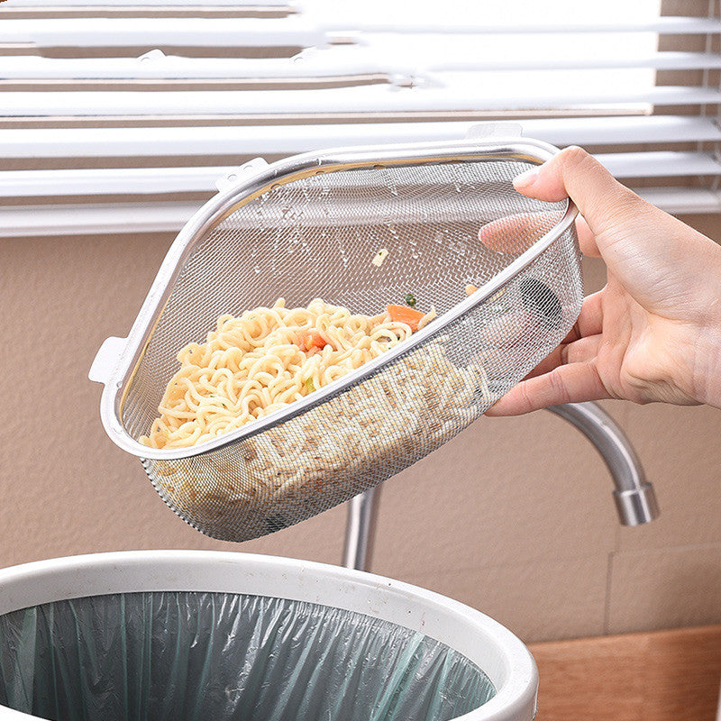 A hand holds a stainless steel mesh noodle strainer basket over a sink, with cooked noodles inside and a trash can visible below.