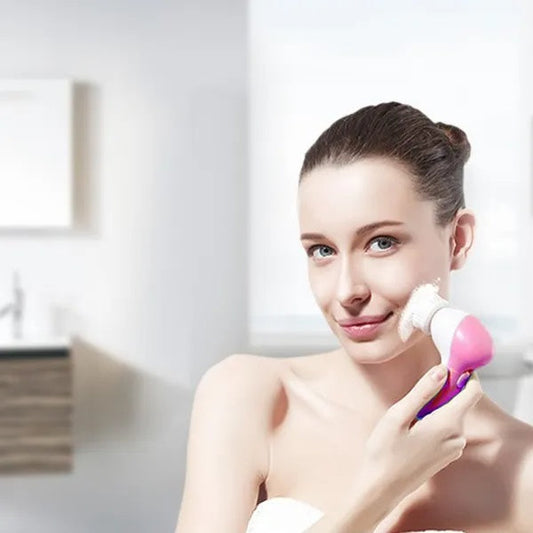 Woman using a pink and purple facial cleansing brush in a bright room.