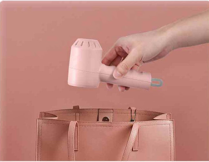 A hand holding a small pink handheld device above a matching pink tote bag, against a solid pink background.